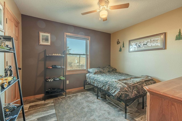 bedroom with ceiling fan, baseboards, a textured ceiling, and wood finished floors