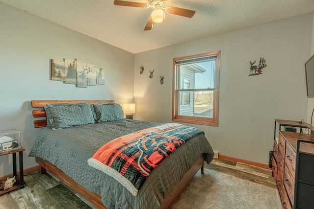 bedroom featuring baseboards, a textured ceiling, wood finished floors, and a ceiling fan