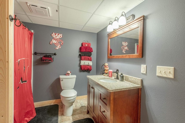 bathroom with visible vents, baseboards, a drop ceiling, toilet, and vanity