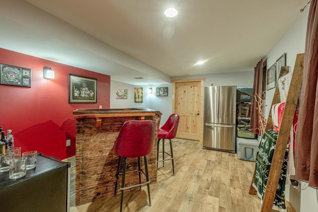 bar featuring a bar, freestanding refrigerator, and wood finished floors