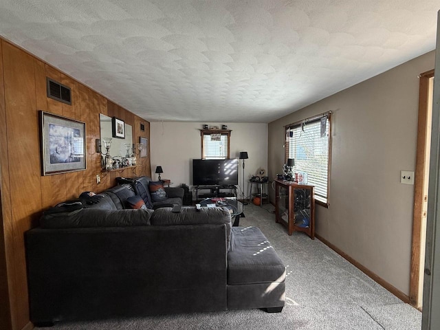 living room featuring visible vents, wooden walls, baseboards, light colored carpet, and a textured ceiling