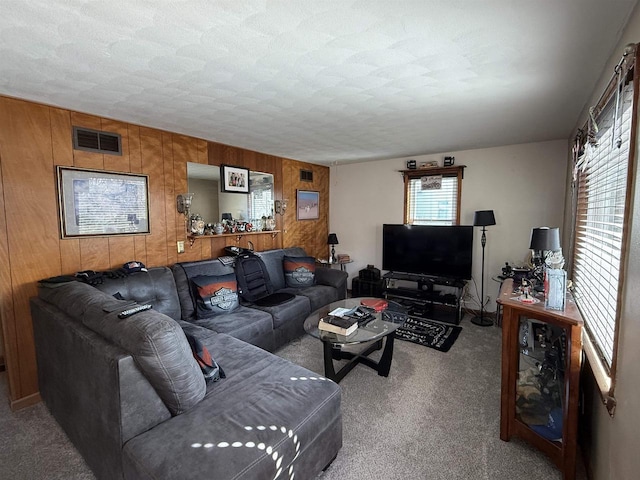 carpeted living area with wooden walls, visible vents, and a textured ceiling