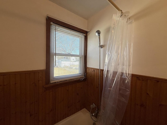 full bathroom featuring wooden walls, shower / bath combo, and a wainscoted wall