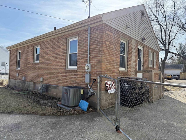 view of home's exterior featuring fence, brick siding, and central AC