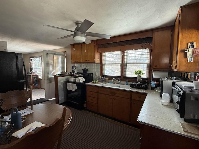 kitchen with black appliances, a sink, brown cabinetry, light countertops, and decorative backsplash