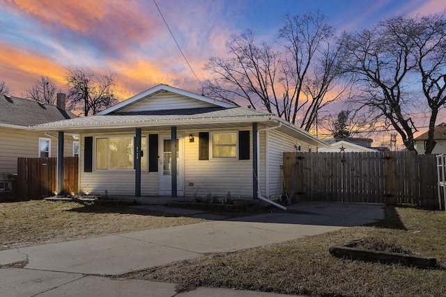 bungalow-style home with covered porch, roof with shingles, and fence