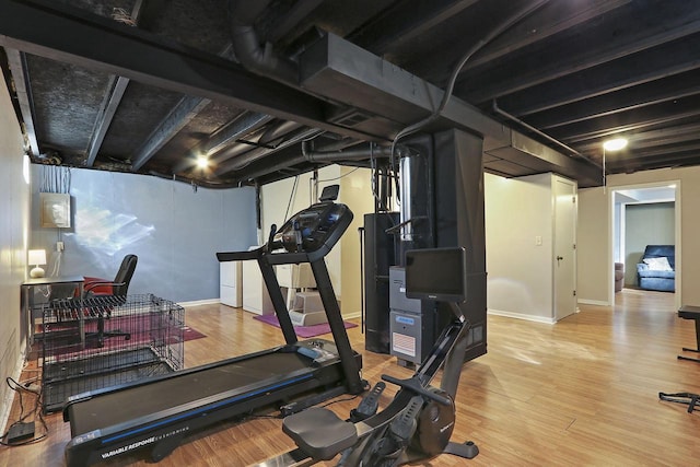 exercise area with baseboards, wood finished floors, and water heater