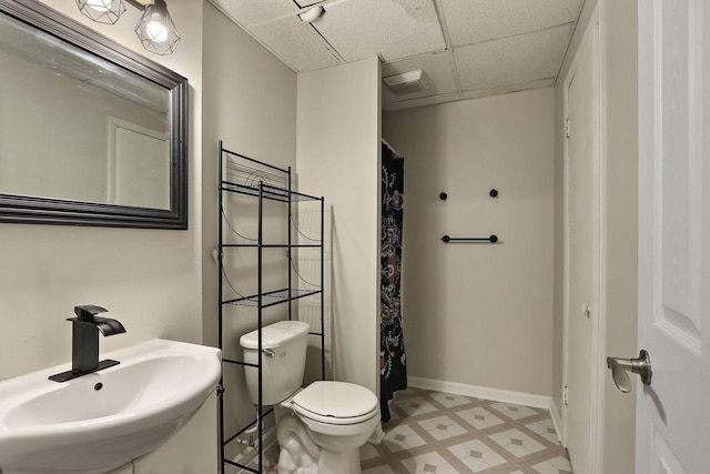 full bath featuring baseboards, a drop ceiling, a sink, tile patterned floors, and toilet