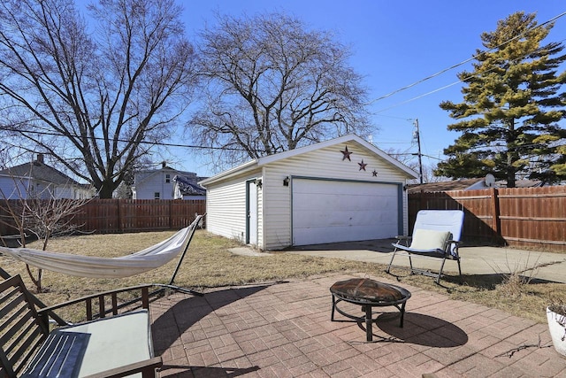 view of patio with a fenced backyard, a detached garage, an outdoor structure, and an outdoor fire pit