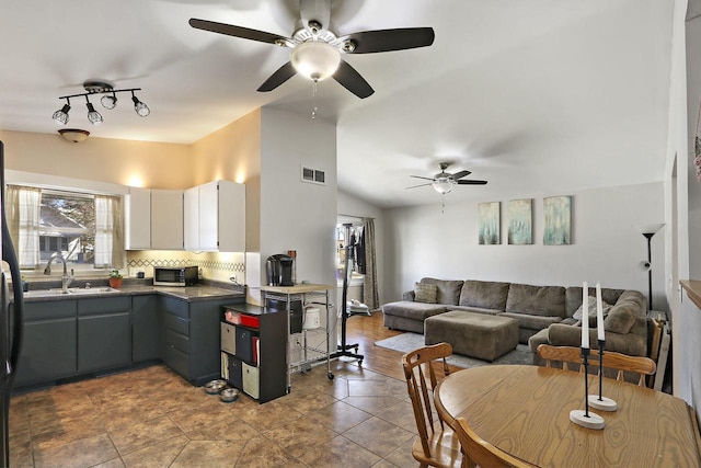 kitchen featuring a sink, decorative backsplash, vaulted ceiling, white cabinetry, and dark countertops