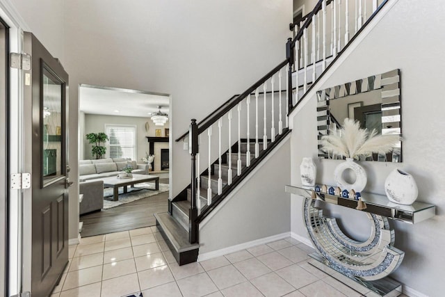 foyer with tile patterned floors, stairway, a fireplace with raised hearth, and a high ceiling