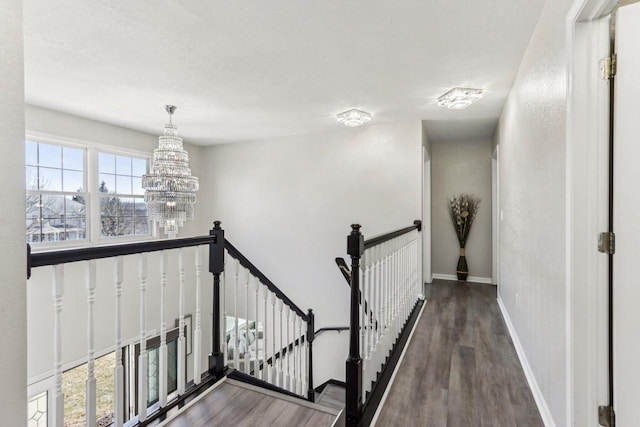 corridor with an upstairs landing, a chandelier, baseboards, and wood finished floors