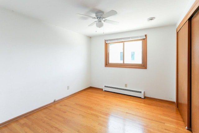 unfurnished bedroom featuring light wood-style flooring, a ceiling fan, a baseboard heating unit, a closet, and baseboards