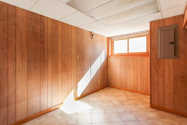 basement with electric panel, baseboards, a paneled ceiling, and wood walls