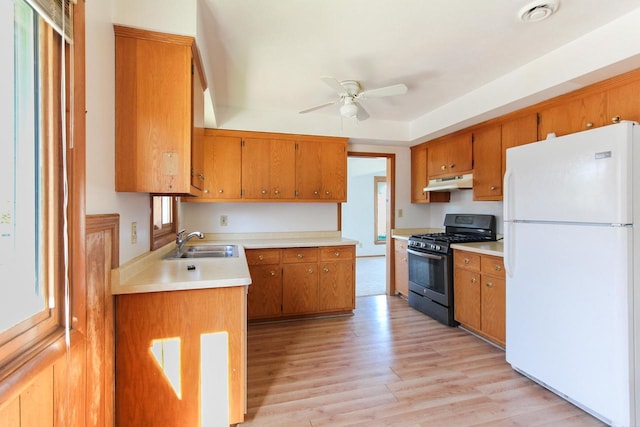 kitchen with under cabinet range hood, a sink, range with gas stovetop, freestanding refrigerator, and brown cabinetry