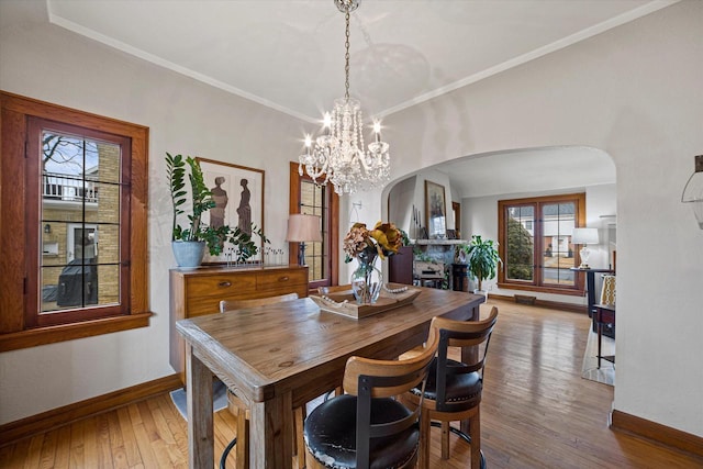 dining room with baseboards, arched walkways, hardwood / wood-style flooring, crown molding, and a notable chandelier