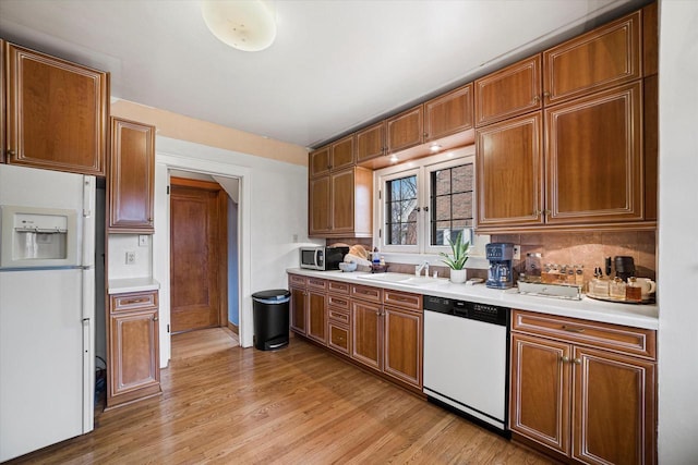 kitchen featuring light countertops, light wood-type flooring, brown cabinetry, white appliances, and a sink