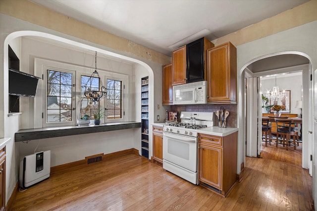 kitchen with visible vents, brown cabinets, a notable chandelier, white appliances, and light wood-style floors