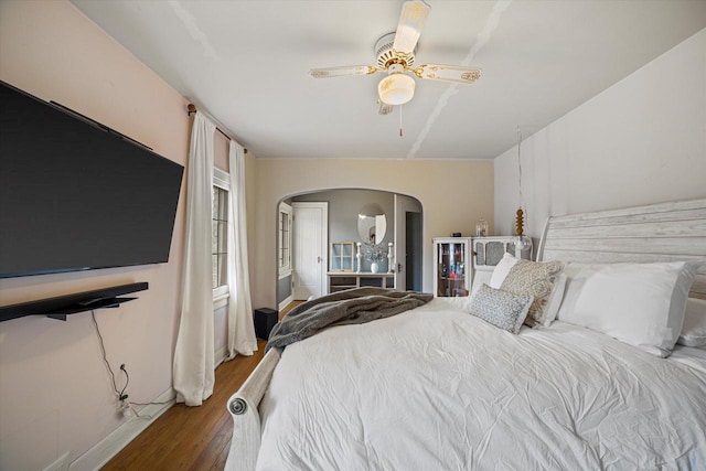 bedroom with arched walkways, a ceiling fan, and wood finished floors