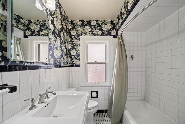 full bath with wallpapered walls, toilet, shower / bath combo, tile walls, and a sink