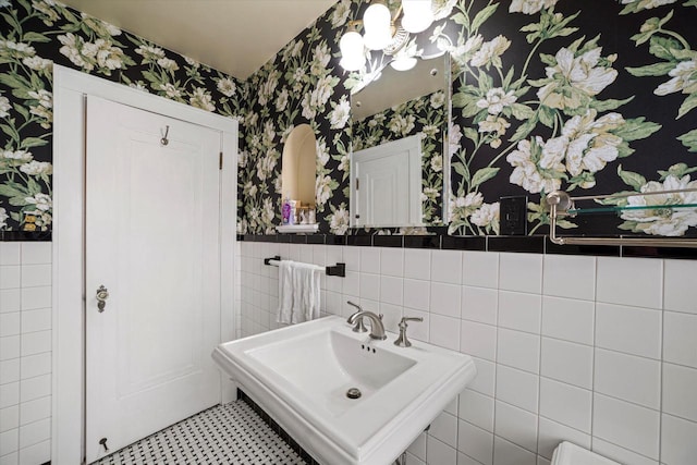 bathroom featuring a sink, a wainscoted wall, tile walls, and wallpapered walls