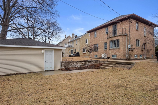 rear view of property featuring a yard, brick siding, and a balcony