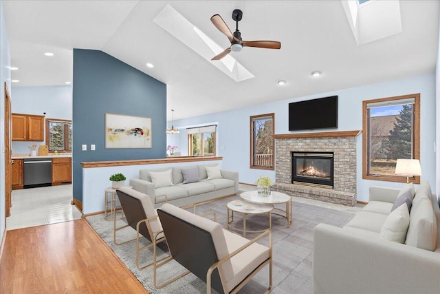 living room with light wood-type flooring, high vaulted ceiling, a skylight, a brick fireplace, and ceiling fan