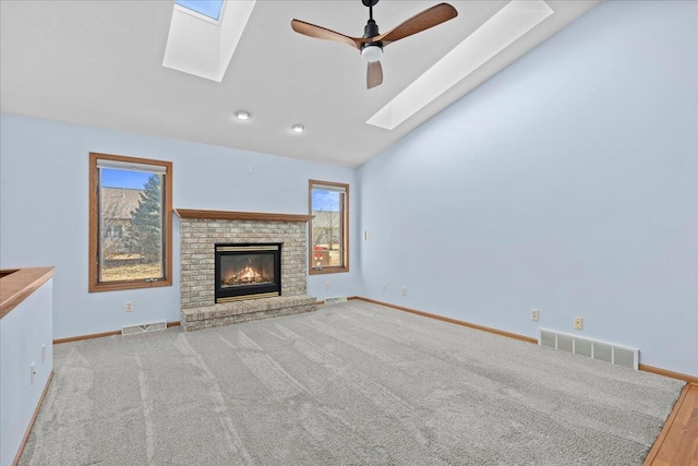 unfurnished living room featuring visible vents, vaulted ceiling with skylight, a fireplace, and ceiling fan