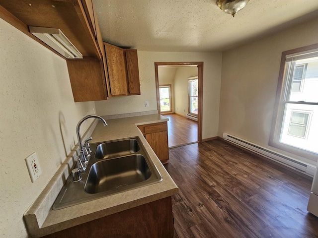 kitchen with a baseboard radiator, brown cabinetry, a sink, a textured ceiling, and dark wood-type flooring
