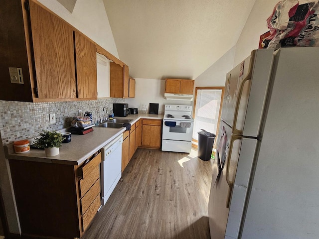 kitchen with a sink, vaulted ceiling, under cabinet range hood, and white appliances