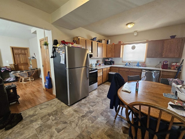 kitchen with stone finish floor, appliances with stainless steel finishes, light countertops, and a sink