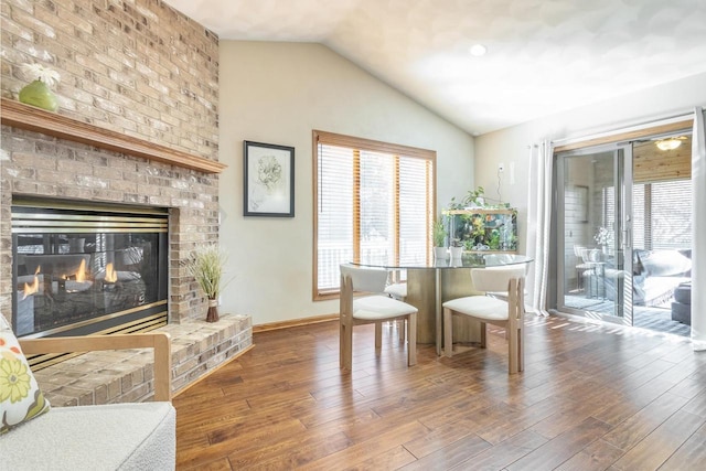 dining space with a fireplace, lofted ceiling, wood finished floors, and baseboards