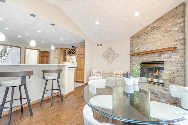 dining area with visible vents, lofted ceiling, stairs, light wood-style floors, and a brick fireplace