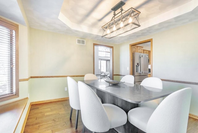 dining space featuring light wood finished floors, visible vents, baseboards, a tray ceiling, and an inviting chandelier