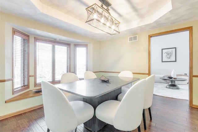 dining area with visible vents, a raised ceiling, hardwood / wood-style floors, an inviting chandelier, and baseboards