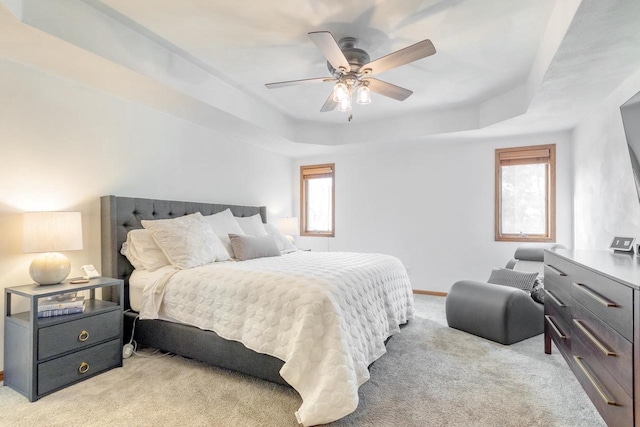 bedroom with light carpet, ceiling fan, baseboards, and a tray ceiling