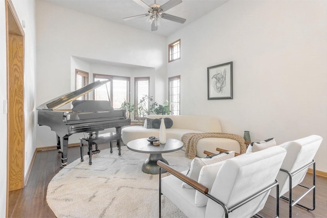 living area featuring a towering ceiling, a ceiling fan, baseboards, and wood finished floors