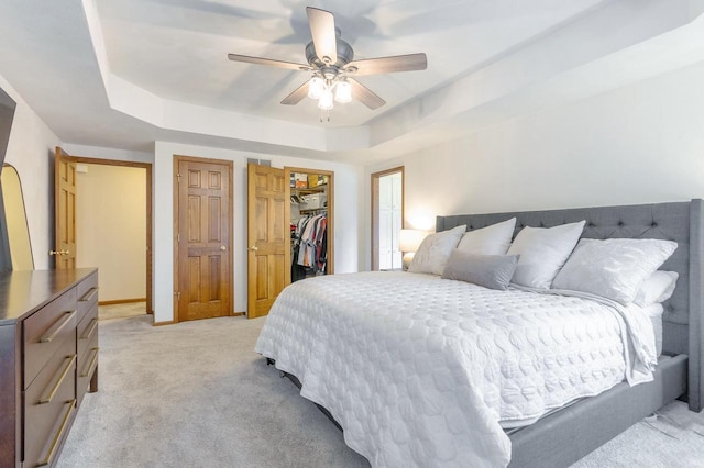 bedroom featuring a spacious closet, ceiling fan, light colored carpet, a closet, and a raised ceiling