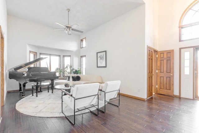 living room with ceiling fan, baseboards, a high ceiling, and dark wood-style floors