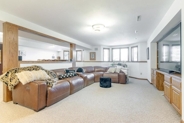 living area with a wealth of natural light, visible vents, baseboards, and light colored carpet