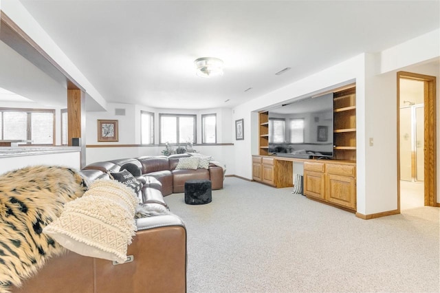 living area featuring built in shelves, baseboards, built in desk, and light carpet