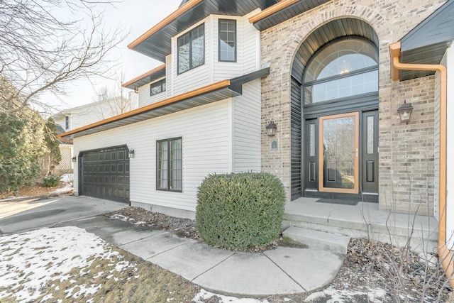 entrance to property featuring a garage, brick siding, and driveway