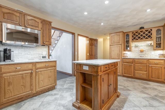 kitchen featuring stainless steel microwave, backsplash, a center island, glass insert cabinets, and open shelves