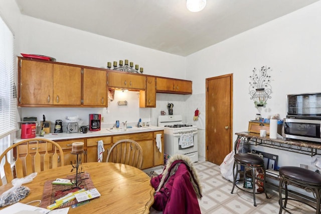 kitchen with white gas stove, a sink, stainless steel microwave, light countertops, and light floors