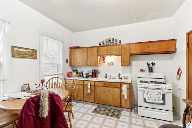 kitchen featuring brown cabinetry, light floors, gas range gas stove, a sink, and light countertops