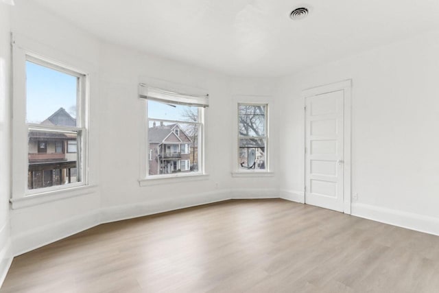 unfurnished room with wood finished floors, visible vents, a wealth of natural light, and baseboards