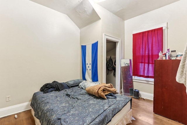 bedroom with vaulted ceiling, baseboards, and wood-type flooring