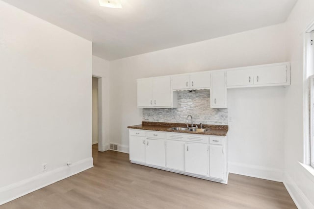 kitchen with dark countertops, visible vents, tasteful backsplash, light wood-style floors, and a sink