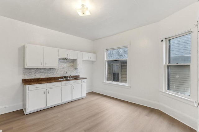 kitchen with a sink, white cabinetry, dark countertops, light wood-type flooring, and backsplash