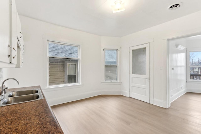 kitchen with white cabinetry, light wood-style flooring, baseboards, and a sink